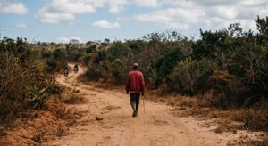 Paysage rural désert de Madagascar, une piste en terre où marche un homme seul de dos, symbolisant l'insécurité et la vulnérabilité face aux réseaux de kidnapping.